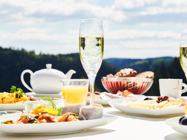 A richly laid breakfast table on the restaurant terrace with a view of the Black Forest in the background.