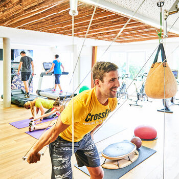 A young man and other guests are training on various sports equipment in a fitness room.