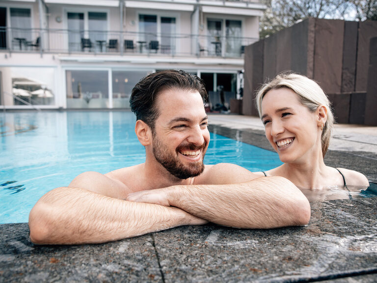 Ein gut gelauntes Paar entspannt zusammen in einem  Aussenpool des Wellnesshotels Berlins KroneLamm