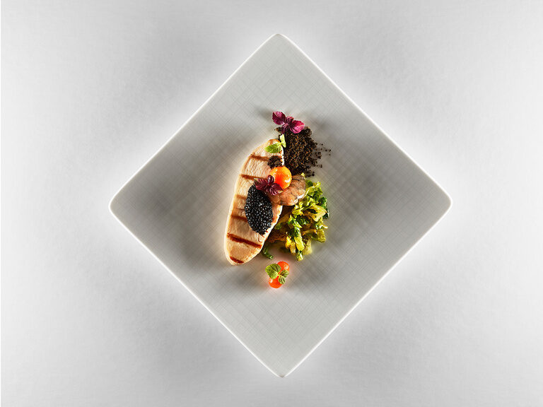 Ein quadratischer Teller auf dem hochwertiges Baguette, Kaviar, sowie eine Garnele exakt angerichtet wurden.
